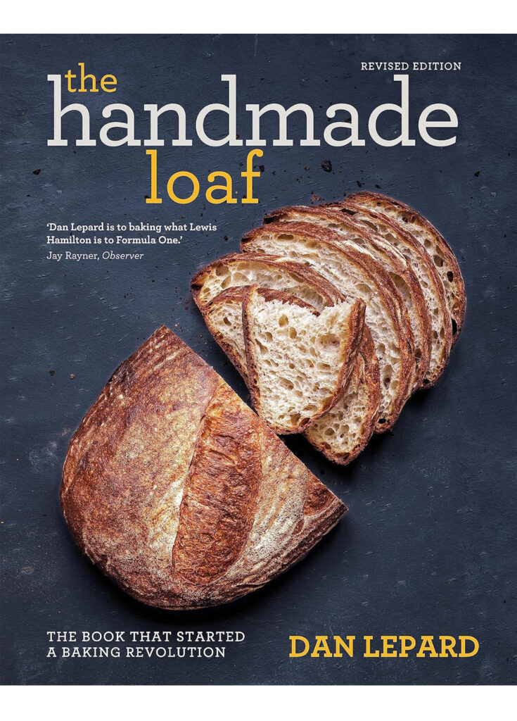 the cover of the handmade loaf, one of dan lepard's award winning cookbooks, showing a cut loaf of bread against a dark grey background